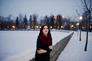 brünettes Mädchen in grünem Pullover und rotem Schal im Freien am abendlichen Wintertag. foto