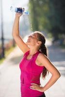 Frau gießt Wasser aus der Flasche auf den Kopf foto