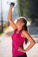 Frau gießt Wasser aus der Flasche auf den Kopf foto