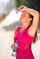 Frau, die nach dem Joggen Wasser aus einer Flasche trinkt foto