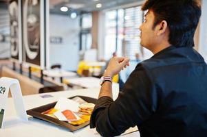 Stilvoller indischer Mann, der im Fast-Food-Café vor seinem Laptop sitzt. foto