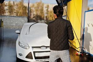 südasiatischer mann oder indischer mann, der seinen weißen transport auf autowaschanlage wäscht. foto