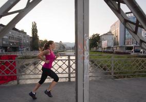 Frau, die am sonnigen Morgen über die Brücke joggt foto