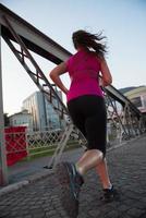 Frau, die am sonnigen Morgen über die Brücke joggt foto