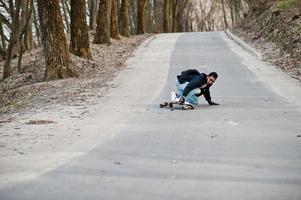 arabischer Streetstyle-Mann in Brille mit Longboard Longboarding die Straße hinunter. foto