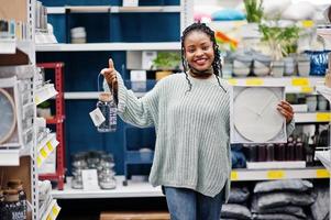 afrikanische frau, die uhr für ihre wohnung in einem modernen einrichtungsgeschäft wählt. foto