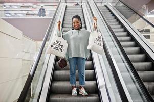 Afrikanerin mit Öko-Einkaufstüten auf Rolltreppe im Einkaufszentrum. foto