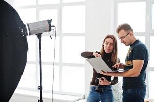 Fotograf erklärt seinem Assistenten im Studio die Aufnahme und schaut auf den Laptop. Teamarbeit und Brainstorming. foto