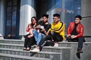 gruppe asiatischer freunde, die auf treppen im freien gegen modernes gebäude sitzen und selfie per telefon machen. foto