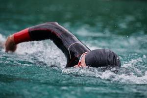 Triathlon-Athlet, der auf dem See schwimmt und einen Neoprenanzug trägt foto