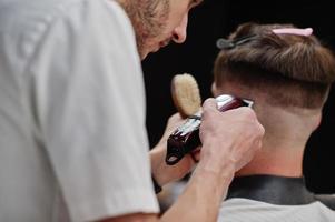 junger bärtiger mann, der vom friseur die haare schneiden lässt, während er im friseursalon auf dem stuhl sitzt. Barbier Seele. foto