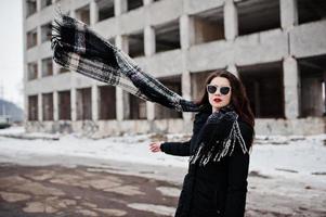 brünettes stilvolles lässiges mädchen in schal und sonnenbrille gegen verlassenen fabrikplatz. Schal in der Luft. foto