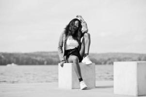 afrikanisch-amerikanisches, dunkelhäutiges, schlankes Model posierte in schwarzen Shorts und Jeansjacke am Meer. foto