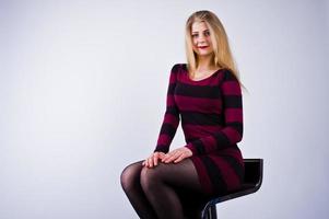 Porträt einer jungen Frau in gestreiftem lila Kleid, die auf dem Stuhl im Studio sitzt. foto