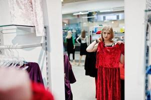Blondes Mädchen probiert ein rotes Kleid in der Boutique an und schaut in den Spiegel. foto