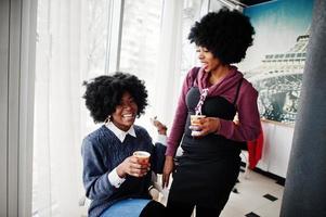 zwei lockige haare afroamerikanerin tragen pullover mit tassen tee, die im café drinnen gestellt werden. foto
