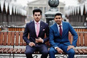 Zwei elegante indische modische Herrenmodelle im Anzug posierten am Wintertag auf der Bank sitzend. foto