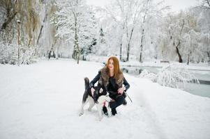 Rothaariges Mädchen, das am Wintertag mit einem Husky-Hund im Park spazieren geht. foto