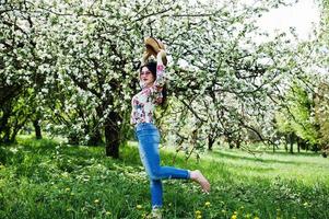 Frühlingsporträt eines brünetten Mädchens mit rosa Brille und Hut im grünen Blütengarten. foto