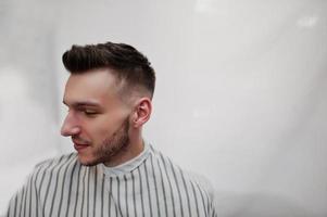 Nahaufnahme des Kopfes eines jungen bärtigen Mannes, der sich im Friseursalon die Haare schneiden lässt. Barbier Seele. foto