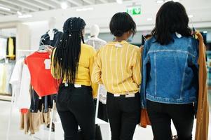 Rückseite von drei afrikanischen Frauen, die Kleidung im Laden auswählen. Einkaufstag. foto