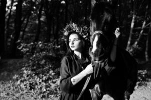 mystisches mädchen in kranzabnutzung in schwarz mit pferd in holz. foto