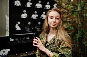 Militärmädchen in Tarnuniform mit Waffe zur Hand vor Armeehintergrund auf Schießstand. foto