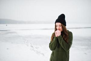 lustige mädchen tragen auf langem grünem sweatshirt, jeans und schwarzer kopfbedeckung, am zugefrorenen see am wintertag. foto