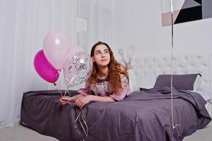 junges mädchen mit luftballons auf dem bett posierte im studiozimmer. foto