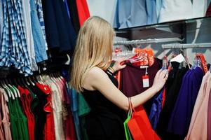 Blondes Mädchen mit Einkaufstüten wählt Kleidung in der Boutique aus. foto