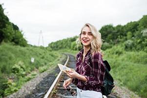 Porträt eines hübschen blonden Mädchens im Tartanhemd, das mit einer Karte in den Händen auf der Eisenbahn spazieren geht. foto