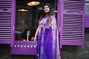 Indisches hinduistisches Mädchen im traditionellen violetten Saree posierte auf der Straße gegen lila Fenster. foto