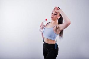 Fröhliche attraktive junge Fitness-Frau in Top und schwarzen Leggings mit Springseil und Flasche Wasser isoliert auf weißem Hintergrund. foto