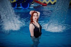 sexy rothaariges Mädchen im schwarzen Badeanzug, das sich im Schwimmbad des Aquaparks ausruht. foto