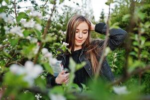 junges brünettes Mädchen in Jeans gegen Frühlingsblütenbaum mit Buch. foto