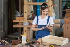 professioneller Zimmermann. Eine Frau arbeitet in einer Tischlerei und verwendet ein Tablet, um Möbel in einem Holzgeschäft zu entwerfen. foto