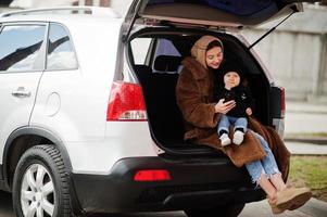 junge mutter und kind sitzen im kofferraum eines autos und schauen auf das handy. Fahrsicherheitskonzept. foto