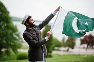 bart pakistanischer mann trägt pakol hut und jacke halten pakistan flagge. foto