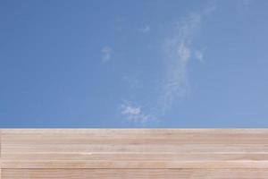 Braune Holztischplatte am blauen Himmel mit Wolkenhintergrund - kann für die Montage oder Präsentation Ihrer Produkte verwendet werden foto