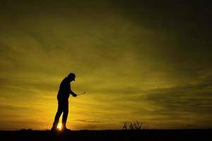 silhouettieren Sie den asiatischen Golfspieler, der Golf während des schönen Sonnenuntergangs spielt foto