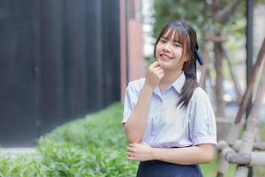 schöne asiatische Oberschülerin in der Schuluniform mit einem selbstbewussten Lächeln, während sie glücklich in die Kamera schaut. foto