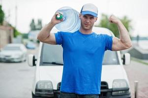 lieferung muskulöser mann im vorderen frachtwagen, der flaschen wasser liefert. foto