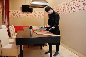 professionelle kochkleidung in schwarz, die sushi und brötchen in einer restaurantküche mit japanischer traditioneller küche herstellt. foto