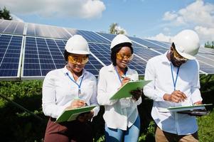 afroamerikanischer techniker überprüft die wartung der sonnenkollektoren. Gruppe von drei schwarzen Ingenieuren, die sich an der Solarstation treffen. foto