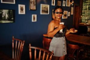 Porträt einer afroamerikanischen Frau, Retro-Frisur, die im Restaurant mit einer Tasse Latte posiert. foto