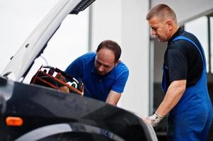 Thema Autoreparatur und -wartung. Zwei Mechaniker in Uniform arbeiten im Autoservice und prüfen den Motor. foto