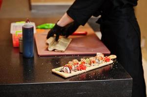 Nahaufnahme der Hände professioneller Köche in schwarzen Handschuhen, die Sushi und Brötchen in einer Restaurantküche mit japanischer traditioneller Küche zubereiten. foto