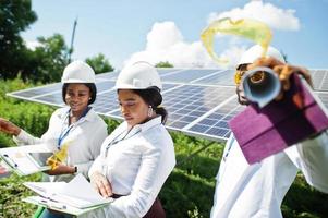 afroamerikanischer techniker überprüft die wartung der sonnenkollektoren. Gruppe von drei schwarzen Ingenieuren, die sich an der Solarstation treffen. foto