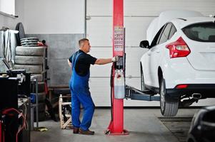 Thema Autoreparatur und -wartung. Mechaniker in Uniform, der im Autoservice arbeitet, Knopf drücken, um Auto anzuheben. foto