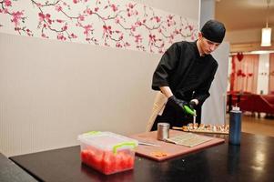 professionelle kochkleidung in schwarz, die sushi und brötchen in einer restaurantküche mit japanischer traditioneller küche herstellt. foto